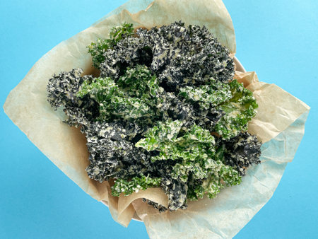 Cooking paper with fresh dehydrated kale chips, hemps seeds, cashew nuts and fresh leaves of kale on bright blue background. flat lay. Eating healthy food.の写真素材