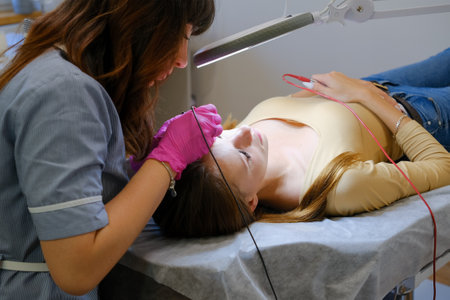 Young woman dermatologist doing hair removal treatment on patients face with electrolysisの写真素材