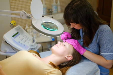Young woman dermatologist doing hair removal treatment on patients face with electrolysisの写真素材