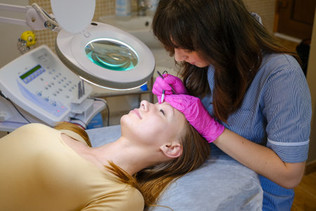 Young woman dermatologist doing hair removal treatment on patients face with electrolysisの写真素材