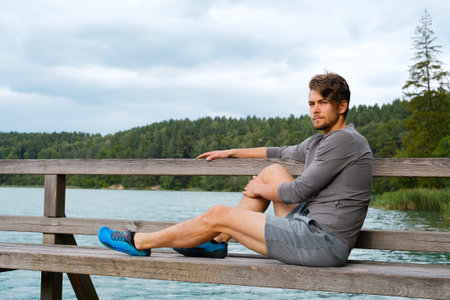 Handsome young man sitting near lake at sunny day. Recreation in nature conceptの写真素材
