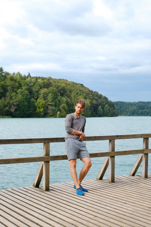 Handsome young man standing near lake at sunny day. Recreation in nature conceptの写真素材