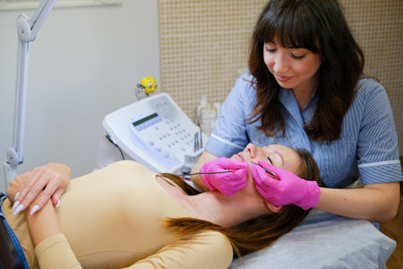 Young woman dermatologist doing hair removal treatment on patients face with electrolysisの写真素材