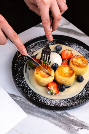 Woman cutting syrniki pancakes with vanilla sauce, berries and ice creamの写真素材