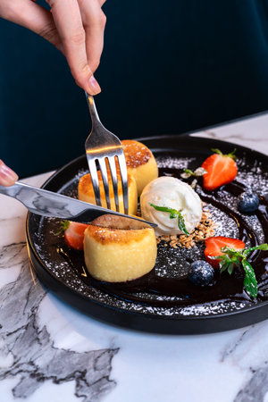 Close-up of hands cutting syrniki dessert with ice cream, berries and sauce