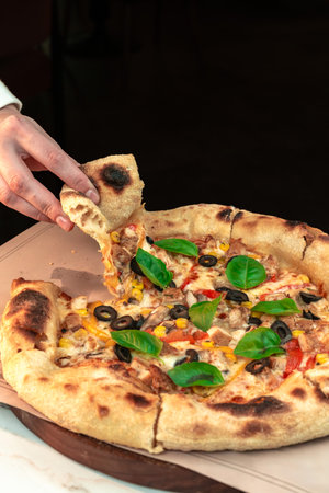 Woman's Hand Lifting a Slice of WoodâFired Neapolitan Pizza on Rustic Table. Fresh, savory moment perfect for restaurant ads, menu visuals and food blogs.の写真素材