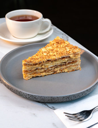 Flaky Napoleon Cake Slice on Plate with Tea. Classic multi layered puff pastry dessert with creamy custard filling. Ideal for cafes, bakery menus, food blogs, and breakfast promotions.の写真素材