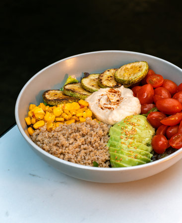 Healthy buddha bowl with hummus, quinoa, avocado, cherry tomatoes, grilled zucchini, corn and...