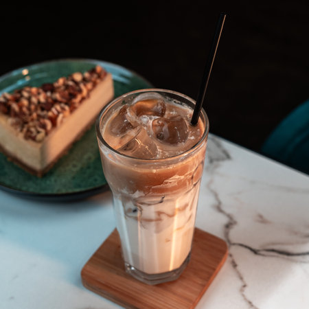 Iced Latte with Layered Milk and Espresso in Tall Glass. Blurred nut cake slice in background. Ideal for cafes, menus, websites, and social media.の写真素材