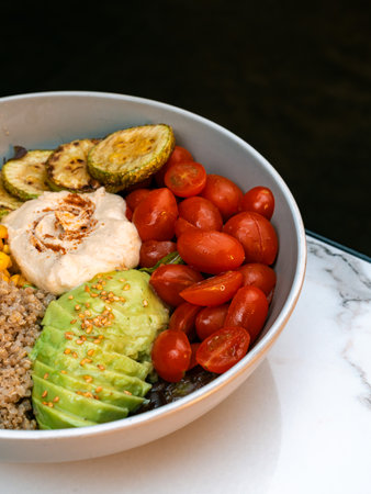 Healthy buddha bowl with hummus, quinoa, avocado, cherry tomatoes, grilled zucchini, corn and sesame. Colorful vegan meal in ceramic bowl. Ideal for plant-based restaurants, nutrition blogs, detox plans, fitness menus and health food advertising.の写真素材