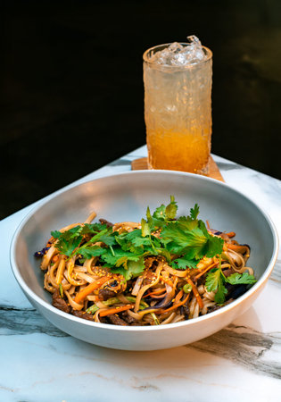 Asian beef udon noodles with vegetables, sesame, and fresh cilantro. Served with iced orange lemonade in a textured glass.の写真素材