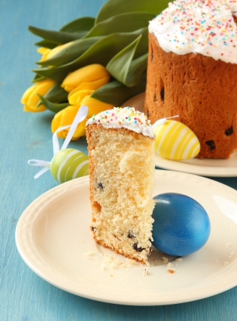 Slice of easter bread with colorful eggs and yellow tulips on blue wooden backgroundの写真素材