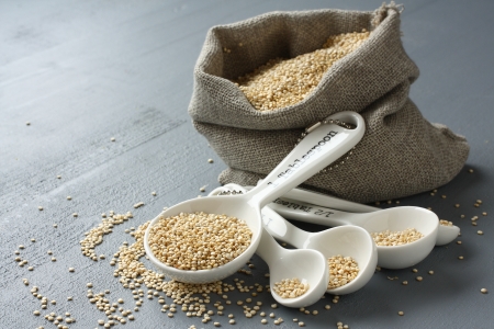 Quinoa grain in small burlap sack and porcelain measuring spoons on gray backgroundの写真素材
