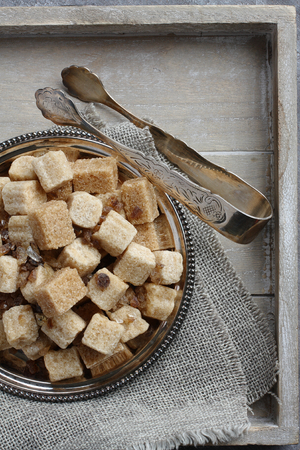 Heap of brown sugar cubes on metal plate on wooden trayの写真素材