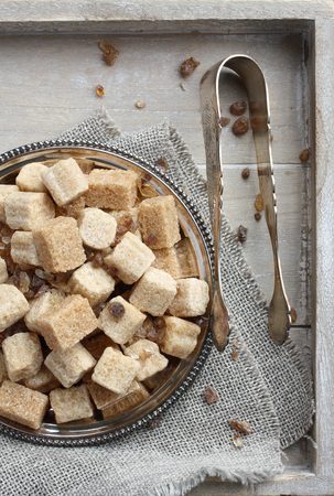 Heap of brown sugar cubes on metal plate on wooden trayの写真素材