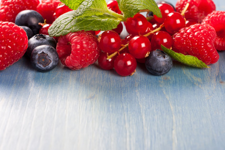 Berries on Blue Wooden Background. Summer or Spring Organic Berry over Wood. Raspberries, Blueberry, Red Currant and Mint. Agriculture, Gardening, Harvest Concept. Copy space.の写真素材