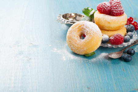 Morning breakfast with mini donuts and berries on plate under powdered sugar on blue wooden background.  Tasty donuts closeup. Doughnut. Copy space.の写真素材