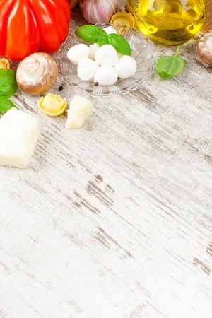 Italian food background, with basil, tortellini, mushrooms, parmesan, mozzarella balls, olive oil, garlic, peppercorns on vintage white wooden table. Background with copy space.の写真素材