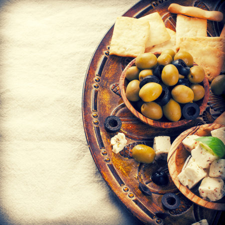 Fresh green olives in olive wood bowl and feta cheese on rustic wooden background.  Selective focus. Food background with copy space. Toned photo.の写真素材