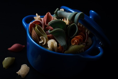 Different types of wholegrain spelt pasta in blue ceramic pot on black background. Selective focus.の写真素材