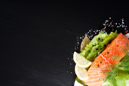 Delicious salmon fillet, rich in omega 3 oil, aromatic spices and lemon on fresh lettuce leaves on black background. Healthy food, diet and cooking background with copy space.の写真素材