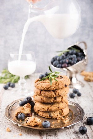 Stack of chocolate chip and blueberries cookies on metal plate with glass of milk decorated with rosemary sprigs. Selective focus.の写真素材