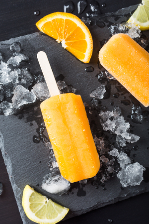 Homemade orange pops with ice and citrus fruits on stone black background. Summer food concept. Top view.の写真素材