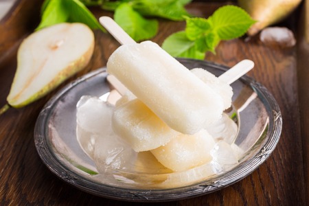 Homemade pear popsicles on metal plate with ice and pears. Summer food concept.の写真素材