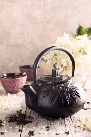 Cast iron black teapot with healthy medicine green tea with elder flower on old white wooden tafel with elder flower branches. Copy space.の写真素材