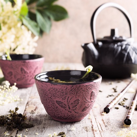 Healthy medicine green tea with elder flower in pink cast iron cup on old white wooden table with elder flower branches. Copy space.の写真素材