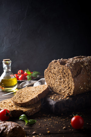 Sandwich preparation. Bread, olive oil, tomato and basil on wooden cutting board. Dark rustic photo...