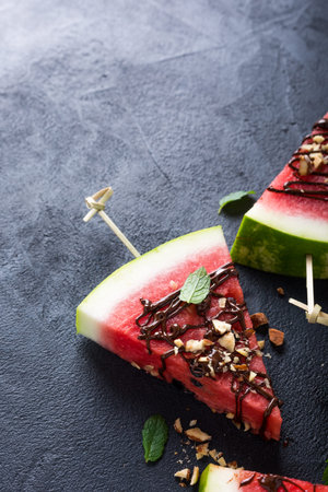 Watermelon slice popsicles with chocolate, nuts and mint on black stone background. Copy space and top view.の写真素材