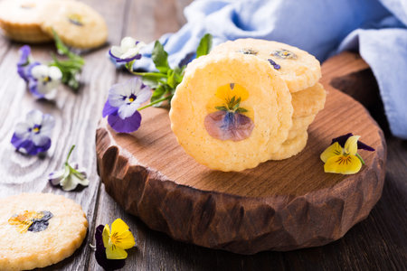 Homemade shortbread cookies with edible flowers on old wooden background. Holiday food