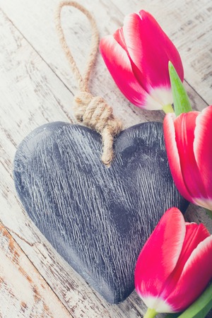 Valentines Day background with decorative heart and pink tulips on white old wooden planks. Valentines Day concept. View from above. Toned photo.の写真素材