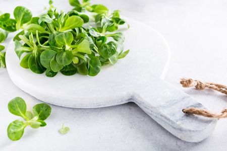 Background with green fresh field salad and marble cutting board on light gray stone table. Healthy food concept with copy space.の写真素材