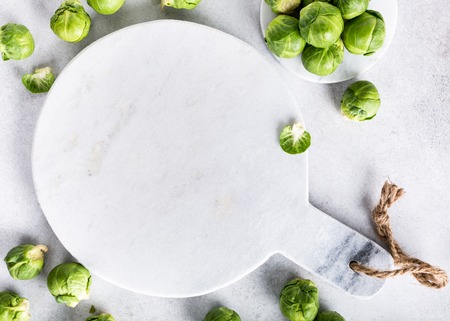 Background with Brussels sprouts and marble cutting board on light gray stone table. Healthy food concept with copy space. Top view.の写真素材