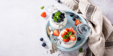 Chia Pudding for breakfast in glass jars garnished with berry in two portions on light gray stone background with a napkin and spoons. Copy space. Top view.の写真素材