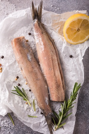 Freshly salted herring with salt, lemon ans rosemary on gray background. Traditional Dutch delicacy. Retro style toned. Top view.の写真素材