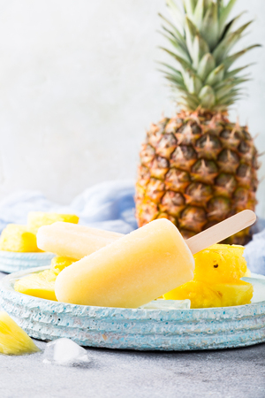 Delicious homemade pineapple popsicles on light blue plate on gray background. Summer food concept with copy space.の写真素材