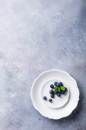 Freshly picked blueberries on white plate on gray stone background. Concept for healthy eating and nutrition with copy space. Top view.の写真素材