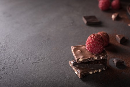 Broken chocolate pieces and raspberries on metal plate on brown background with copy space. Dark photo.の写真素材