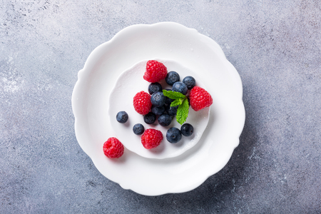 Freshly picked blueberries and raspberries on white plate on gray stone background. Concept for healthy eating and nutrition with copy space. Top view.の写真素材