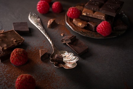 Broken chocolate pieces and raspberries on brown background with copy space. Dark photo.の写真素材