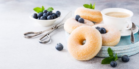 Doughnuts with powdered sugar, cup coffee and fresh blueberries on light gray background. Selective focus. Copy space.の写真素材