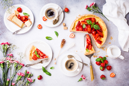 Overhead shot of cups of coffee, delicious homemade strawberry cheesecake and flowers on light gray background. Top view, flat lay.の写真素材