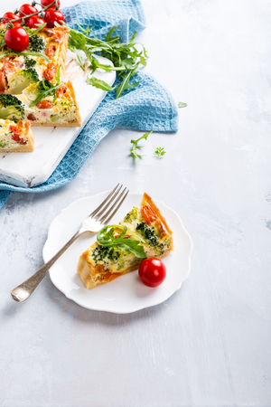 Slice of delicious vegetarian homemade quiche with cherry tomatoes and broccoli on white plate. Healthy food concept with copy space.の写真素材