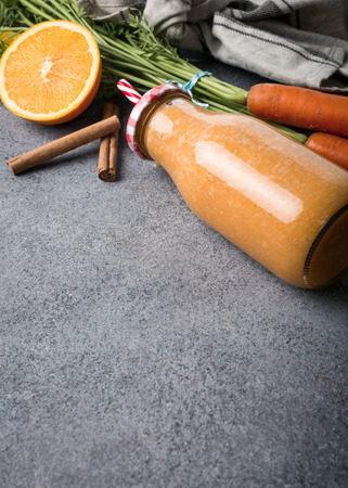 Healthy carrot smoothie with orange and cinnamon in glass bottle and ingredients. Detox, diet, healthy, vegetarian food concept with copy space.の写真素材