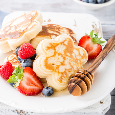 Scotch pancakes in flower form with berries and honey on white wooden background. Healthy breakfast concept.の写真素材