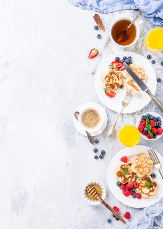 Flat lay with breakfast with scotch pancakes in flower form, berries and honey on light wooden table. Healthy food concept with copy space.の写真素材