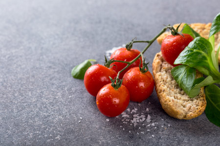 Gray stone background with cherry tomatoes, wholewheat rusks and corn salad. Healthy food concept...